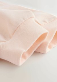 Soft, light pink cotton fabric, featuring a smooth texture and ribbed cuffs, draping gently over a plain surface.