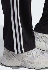 Svarta träningsbyxor med vita sidostriper, kombinerat med vita sneakers med nät- och texturdetaljer, dämpade sulor och snörning.