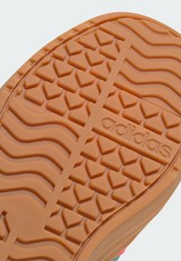 Suola in gomma con una superficie arancione testurizzata, caratterizzata da un motivo a zigzag e con il marchio "adidas" in rilievo lungo il bordo.