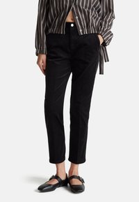 Zwarte corduroy broek met een rechte pasvorm, voorzien van zijzakken en een hoge taille. Draagt een gestreepte button-up shirt en zwarte schoenen.