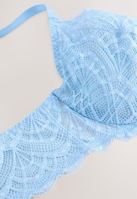 Šviesiai mėlynas nėriniuotas liemenėlė su sudėtingais gėlių raštais, banguotais kraštais ir reguliuojamomis petnešėlėmis, atspindinti subtilų ir tekstūruotą dizainą.