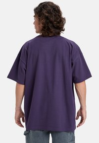Lilla oversized t-shirt med korte ærmer, rund halsudskæring og en glat bomuldsstruktur. Synlige syninger og afslappet pasform.