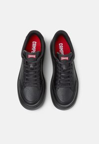 Sneaker nere con tomaia in pelle testurizzata, punta rotonda e lacci neri. Soletta rossa con il marchio "CAMPER" sulla linguetta.