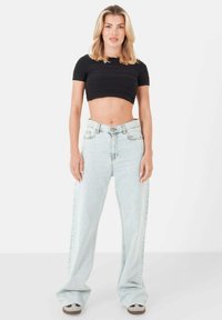 Jeans azzurri chiari a vita alta con gamba larga, abbinati a un top nero aderente e corto. L'outfit presenta una vestibilità casual e rilassata.