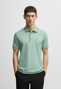 Mint green polo shirt with short sleeves, two-button placket, and a contrasting black collar trim. Features a small brand logo on the chest.