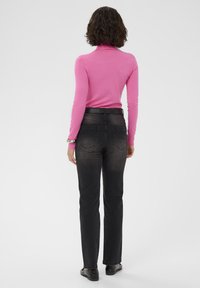 Pull ajusté à col roulé rose et jean en denim noir, avec une ceinture standard et des poches arrière, vus de dos.