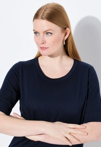 Krajkový top s krátkým rukávem v námořnické modré barvě, kulatým výstřihem, hladkou texturou a přiléhavým střihem, s jemnými detaily šití.
