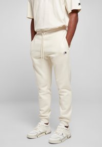 Pantalones de chándal color crema con una cintura elástica y cordón, bolsillos laterales y un pequeño logo negro. Combinados con zapatillas blancas con detalles en gris.