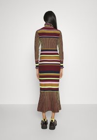 Ribbad långklänning med en mock-neck, där vertikala ränder i flerfärgat burgundy, grönt och rosa pryder plagget, och med en utsvängd nederkant.