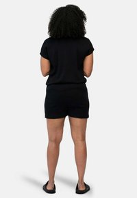 Zwarte top met korte mouwen, gecombineerd met zwarte shorts, beide gemaakt van een gladde stof. Draagt zwarte instappers. Uitzicht van achter.