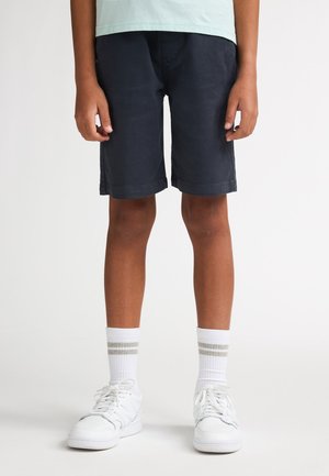 Marineblauwe korte broek met een gladde textuur en opgerolde zomen, gecombineerd met witte sokken met grijze strepen en witte sneakers.