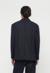 Veste cintrée en laine texturée à rayures marines. Elle se distingue par une fente simple, un revers cranté et des boutons aux manches. Ajustement slim avec une finition lisse.