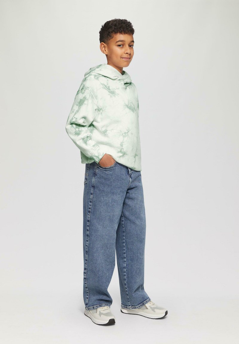 Groene tie-dye hoodie met lange mouwen, relaxed fit en een kangoeroezak, gedragen met losse blauwe jeans en lichte sneakers.