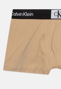 Beige Calvin Klein boxershorts met een zwarte elastische tailleband waarop de merknaam in het wit staat. Zachte katoen, gladde textuur.