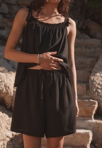 Black sleeveless top with ruffled neckline and adjustable straps, paired with matching black shorts featuring an elastic waistband and drawstring.