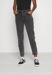 Svart bodysuit kombinerat med högmidjade grå jeans. Jeansen har en klassisk design med fem fickor och ett något avsmalnande ben. Svarta sneakers.