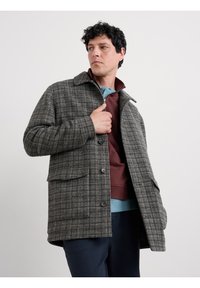 Grauer kariertet Blazer mit einem Kragen-Design, ausgestattet mit gro�ßen Taschen, Knopfverschlüssen und einem strukturierten Stoff. Geknöpft über einem burgunderfarbenen Sweatshirt getragen.