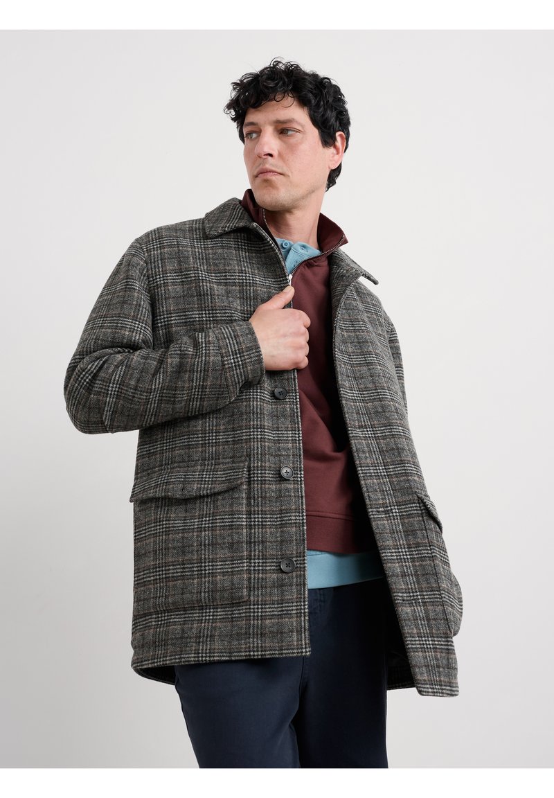 Grauer kariertet Blazer mit einem Kragen-Design, ausgestattet mit großen Taschen, Knopfverschlüssen und einem strukturierten Stoff. Geknöpft über einem burgunderfarbenen Sweatshirt getragen.