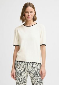 Cremefarvet kortærmet sweater med sort bølget kant ved hals og ærmer. Kombineret med mønstrede bukser i sort og hvid med blomsterdesign.