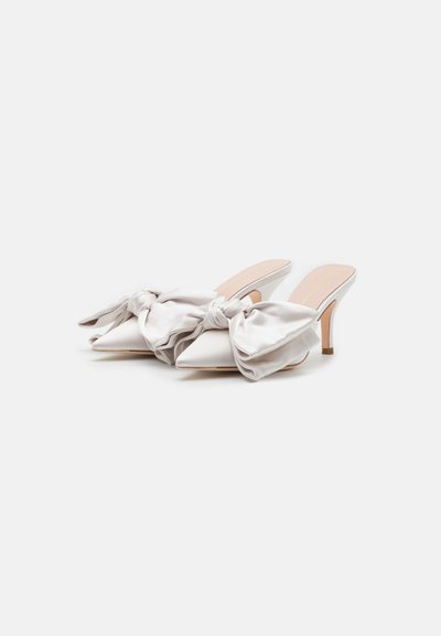 White satin mules with pointed toes and a pronounced large bow on the front, featuring a slender, low heel. Smooth texture, elegant design.