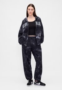 Czarna bluza tie-dye z napisem "NIGHTMARE", zestawiona z pasującymi dresami. Tkanina wygląda na miękką; oba elementy mają elastyczne mankiety i sznurki do regulacji.