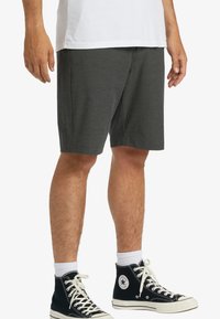 Bermudas grises de tela suave, a la altura de la rodilla y con corte recto. Combinadas con zapatillas negras de caña alta y calcetines blancos.