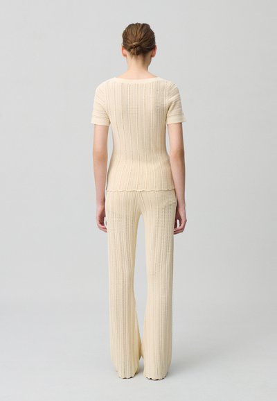 Ensemble en tricot deux pièces crème, avec des manches courtes et un tricot texturé. Le haut a un ourlet festonné, associé à un pantalon à jambes larges.