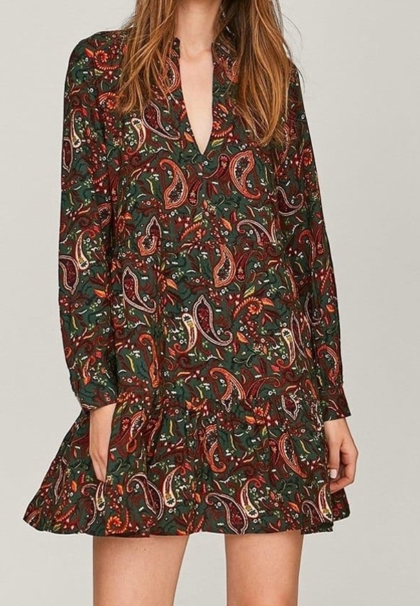 Langärmliges Kleid in Dunkelgrün mit einem Paisleymuster in Rot, Weiß und Gelb. Verfügt über einen tiefen V-Ausschnitt und einen gestuften Rock.