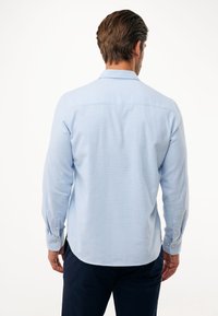 Lichtblauw longsleeve overhemd met knoopmanchetten, afgeronde zoom en een textuurstof. Achteraanzicht toont een gladde kraag en naaddetails.
