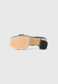 Svart hæl sandal med glatt overdel, bred stropp og teksturert beige gummisåle med horisontale riller. Fyrkantet hælform.