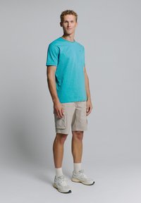 Turquoise katoenen t-shirt met ronde hals, gecombineerd met beige cargoshorts. Lichte sneakers met grijze accenten maken de casual outfit compleet.