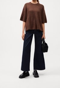 Pull court à manches courtes marron, en tissu pelucheux, avec un ourlet droit ; assorti à un jean large en denim foncé. Sac noir et mocassins épais complètent le look.