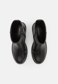 Bottines noires en cuir lisse, avec une fermeture éclair sur le côté, un bout rond et une semelle en caoutchouc. Pas de motifs ou d'accents visibles.