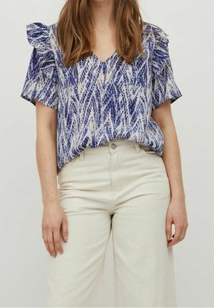 Mujer con blusa de manga corta azul y blanca con estampado, metida dentro de pantalones crema de talle alto y pierna ancha, sobre un fondo liso.