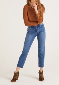 Camicia marrone con bottoni, jeans blu a vita alta con orlo sfrangiato e stivaletti con stampa leopardata e tacco a blocco.