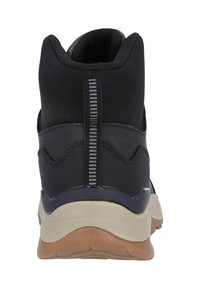 Svart sportskor med en strukturerad ovandel, med en kontrasterande ljusbrun sula. Vertikala vitstrimmiga detaljer på baksidan.