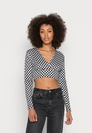 Top cropped em preto e branco com padrão xadrez, mangas longas, decote em V profundo e design justo, combinado com jeans pretos de cintura alta.