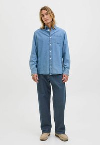 Hele sinine teksashirt, millel on nuppude esiosa, üks rinna tasku ja pikad varrukad, kombineerituna tumedate siniste lagedate pükstega ning beežide kingadega.