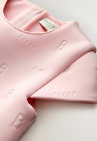 Hellrosa Kleid mit geprägten Mustern "BAKER" und "B". Glatter Stoff mit rundem Ausschnitt und Reißverschluss auf der Rückseite.