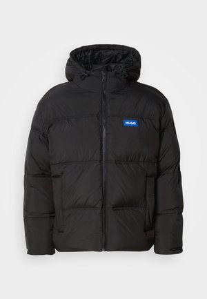 Giubbotto imbottito nero con cappuccio, chiusura zip frontale e due tasche laterali. Presenta pannelli cuciti e un logo blu "HUGO" sul petto.