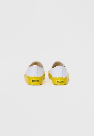 Baltas audekla slip-on apavi ar teksturētu dzeltenu gumijas zoli. Papēžā ir melna "Moschino" logo. Vienkāršs dizains bez rakstiem.