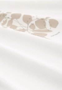 Tissu blanc à texture lisse, présentant un subtil motif floral beige et blanc le long d'un bord.