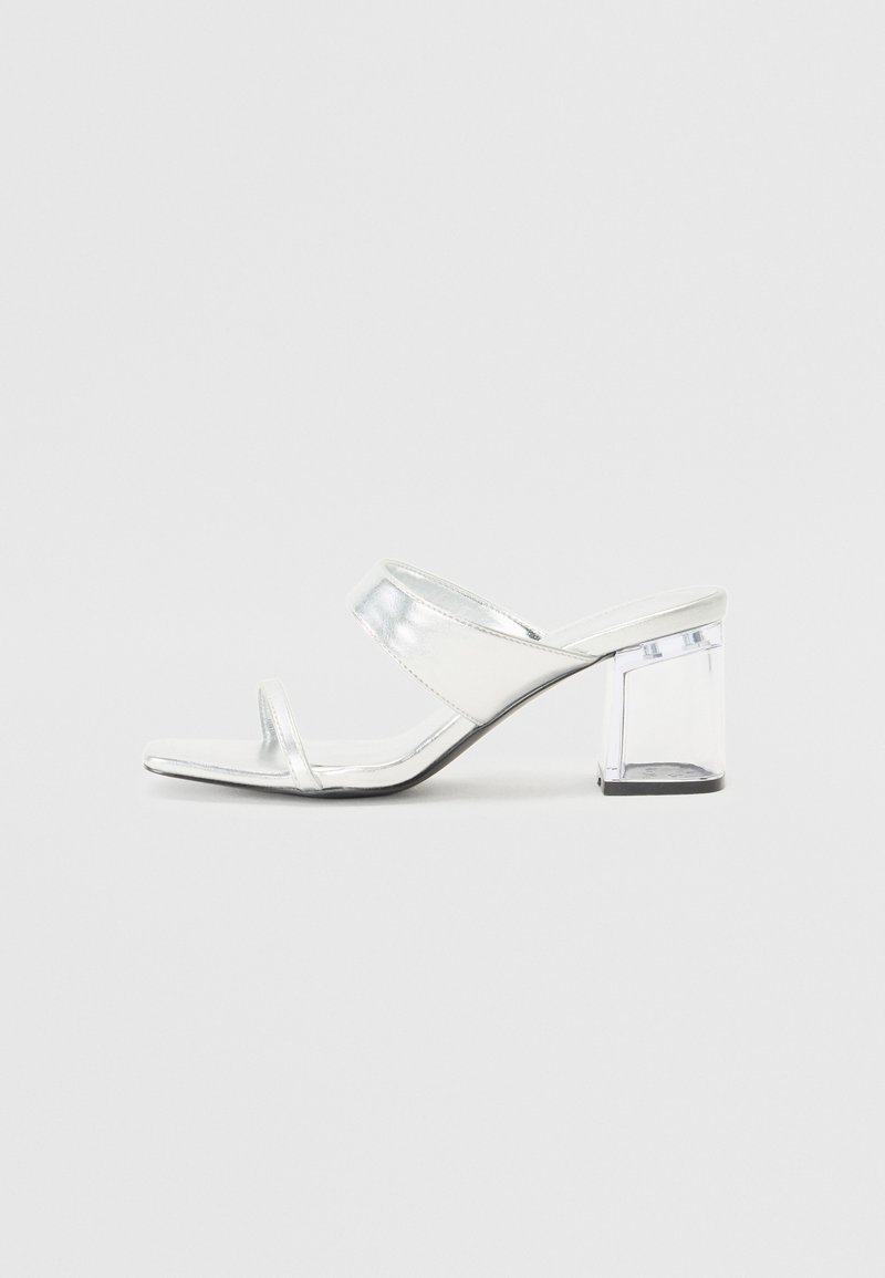 Sandales à talons métalliques argentées avec deux fines brides, bout ouvert et un talon bloc transparent. Surface lisse et design minimaliste.