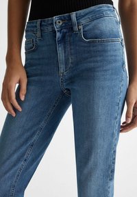 Jeans de mezclilla azul con un ajuste slim, con una cintura de altura media, cinco bolsillos y áreas sutilmente descoloridas. La tela es suave y lisa al tacto.