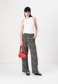 Top sans manches blanc, pantalon large à motif zèbre noir et blanc, casquette noire, sac à main rouge et chaussures plates noires avec des accents.