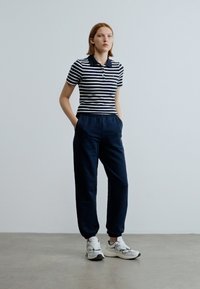 Ριγέ πόλο μπλουζάκι σε ναυτικό μπλε και λευκό, συνδυασμένο με ναυτικό μπλε αθλητικό παντελόνι και λευκά αθλητικά παπούτσια. Λείες υφές και άνετη εφαρμογή.