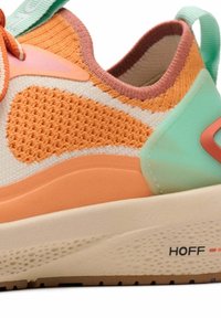 Baskets avec une tige en mesh de couleur crème clair, présentant des accents orange et vert menthe. Semelle épaisse crème avec motif texturé et détail de logo.