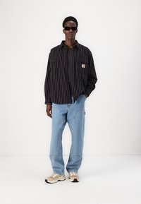 Black and white striped button-up shirt, gray top underneath, light blue baggy jeans, and beige sneakers. Features two chest pockets.