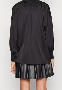 Czarna bluzka z długimi, bufkowatymi rękawami, marszczonym dekoltem oraz plisowaną czarną skórzaną spódnicą. Gładka faktura z elastycznymi mankietami.