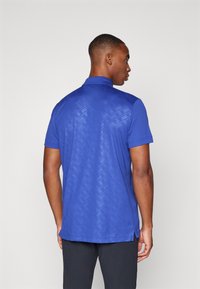 Blå polo skjorte med korte ermer som har en teksturert bakside med et geometrisk mønster og sidedelinger for bedre bevegelsesfrihet.